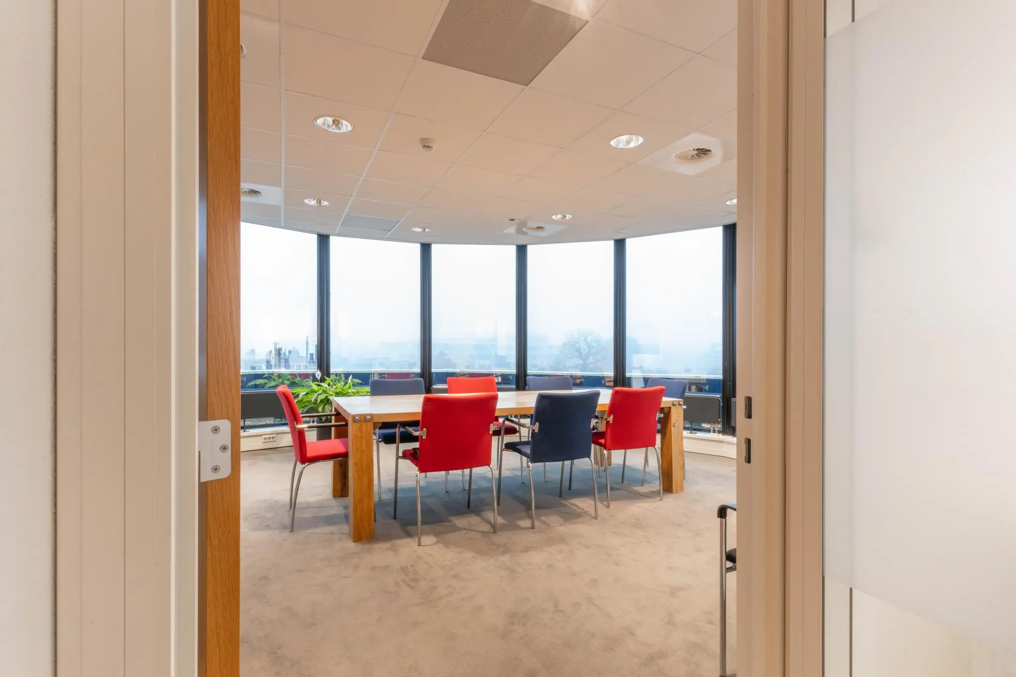 Vergaderruimte met kleurrijke stoelen en grote ramen aan de 1e Hogeweg.